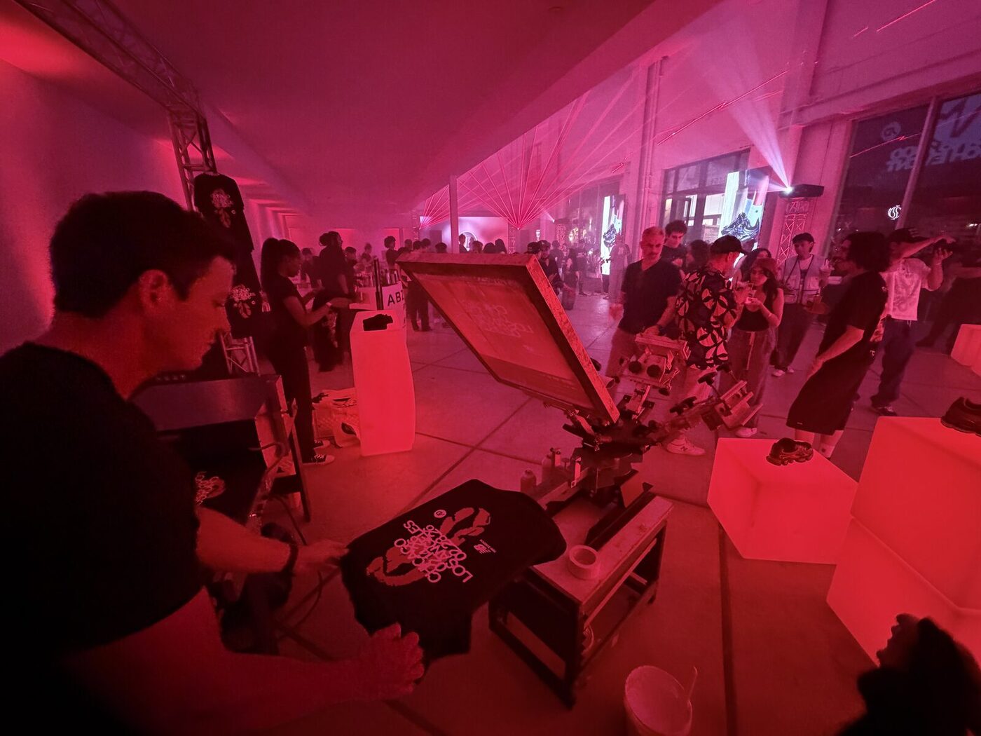 Merch Troop live screen-printing station running at a night event, crowd and stage lighting in the background